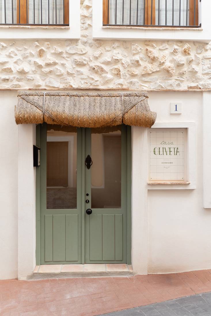 The green double door beneath the esparto blind, with the tiled house sign.