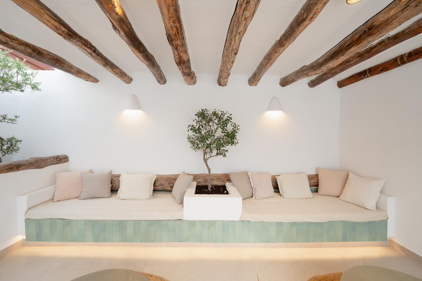 The roof terrace by day: a long bench beneath the beams, linen cushions, an olive tree and two low tables.
