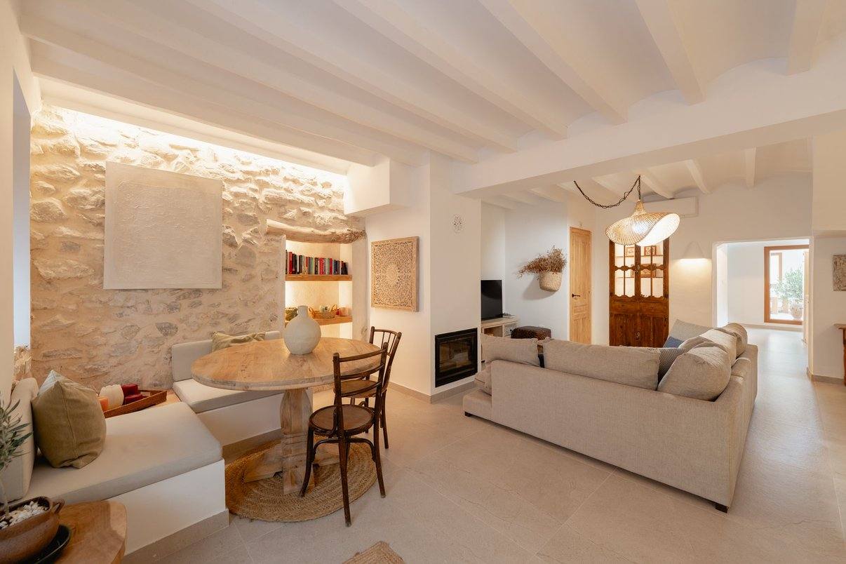 The sitting room: lit stone wall, round table, linen sofa and fireplace.